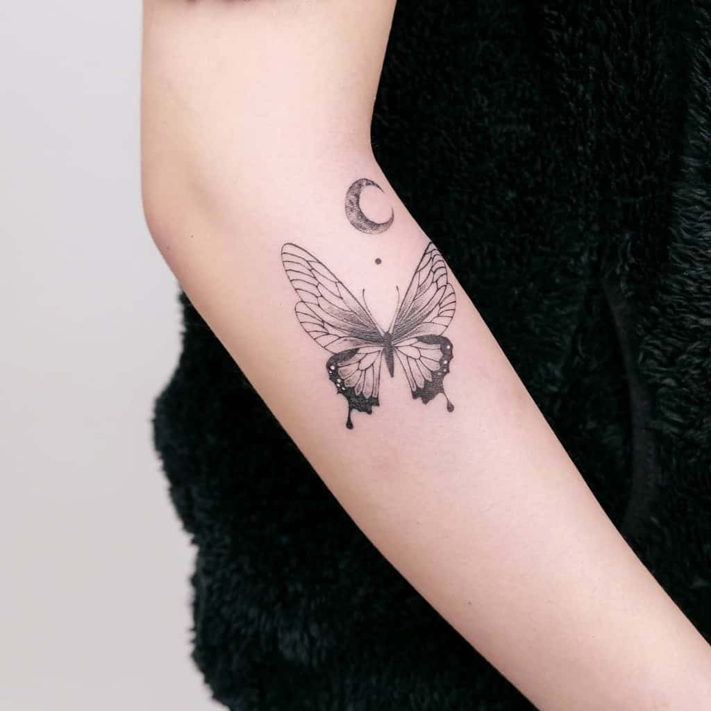 Minimalist outer forearm tattoo featuring a delicate butterfly with a crescent moon above, symbolizing transformation and intuition