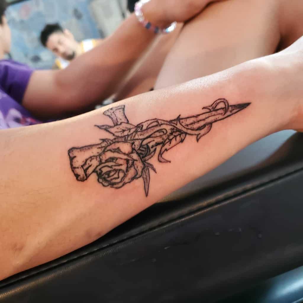 An outer forearm tattoo featuring a rose entwined with thorns and a cross