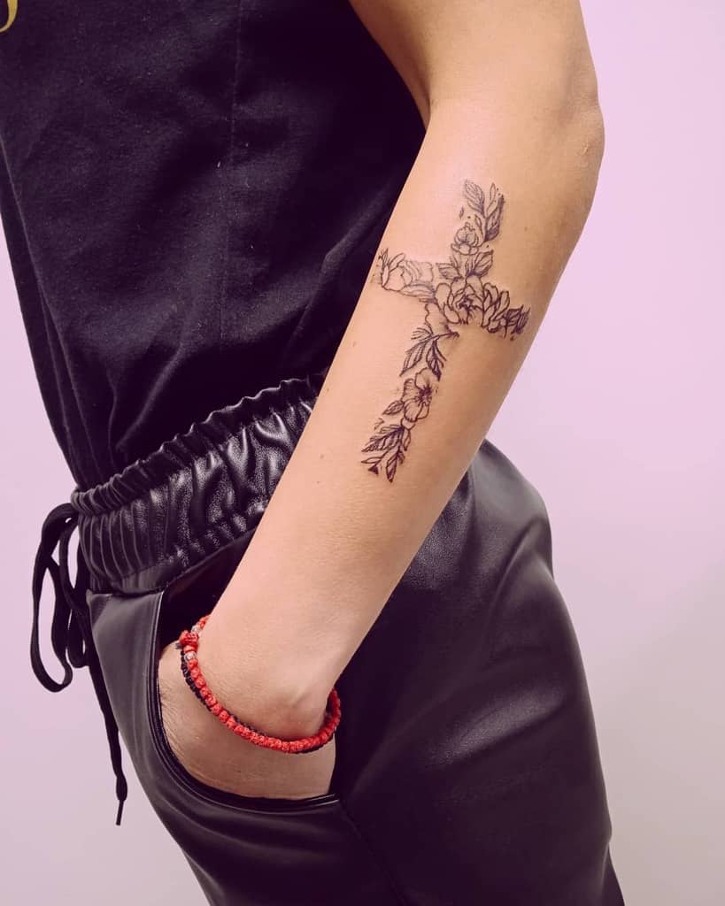 Outer forearm tattoo featuring a cross formed by delicate floral elements, symbolizing faith and growth