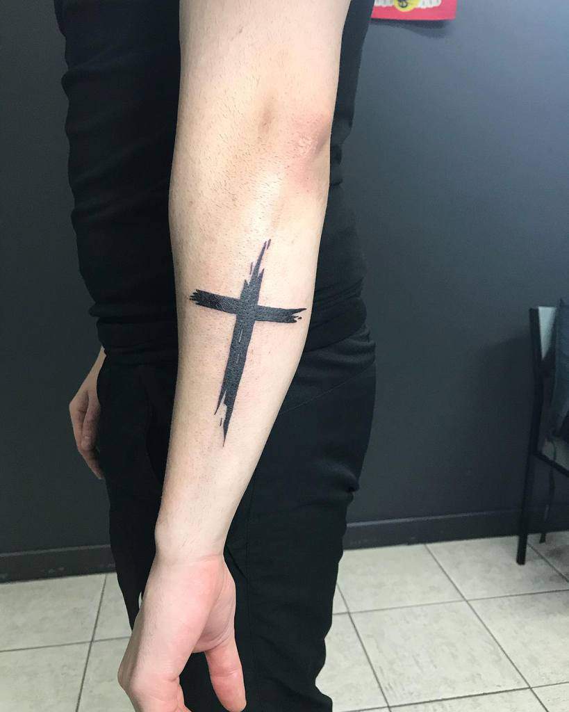 A striking forearm tattoo of a bold, brushstroke-style cross