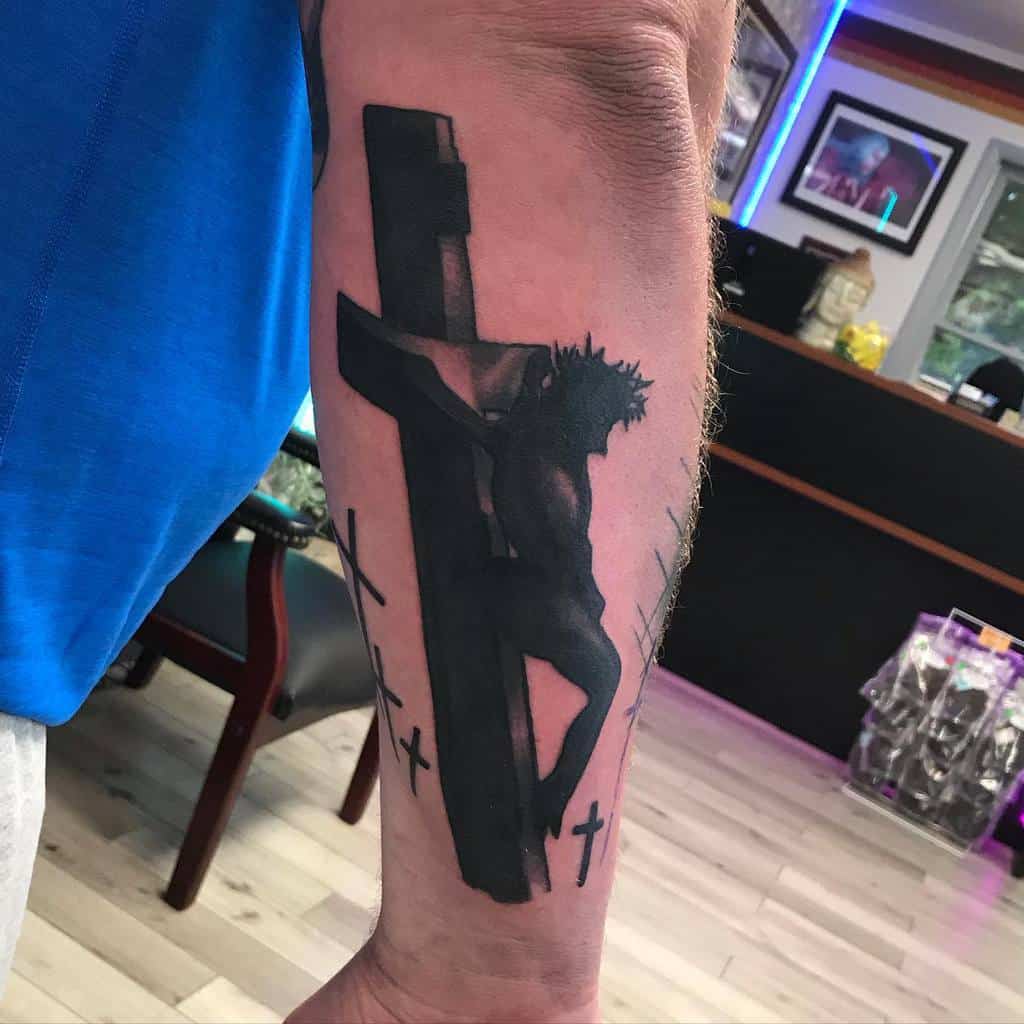 Outer forearm tattoo of Jesus on the cross, depicted in black and gray tones, symbolizing sacrifice and faith