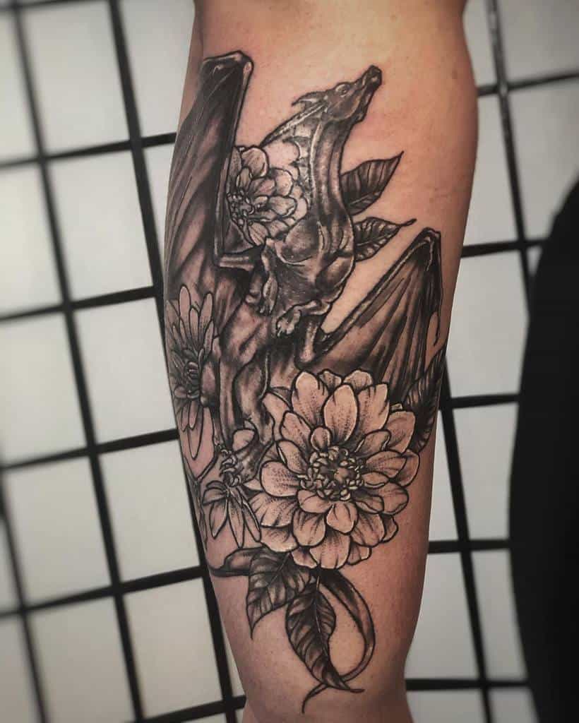 Outer forearm tattoo of a dragon intertwined with large flowers in black and gray shading, symbolizing power and beauty