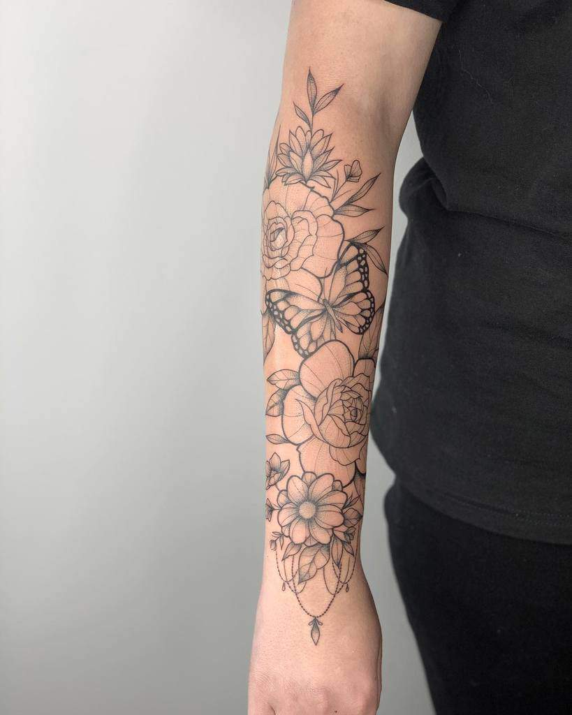 Outer forearm tattoo featuring detailed linework of flowers and a butterfly, symbolizing growth, beauty, and transformation