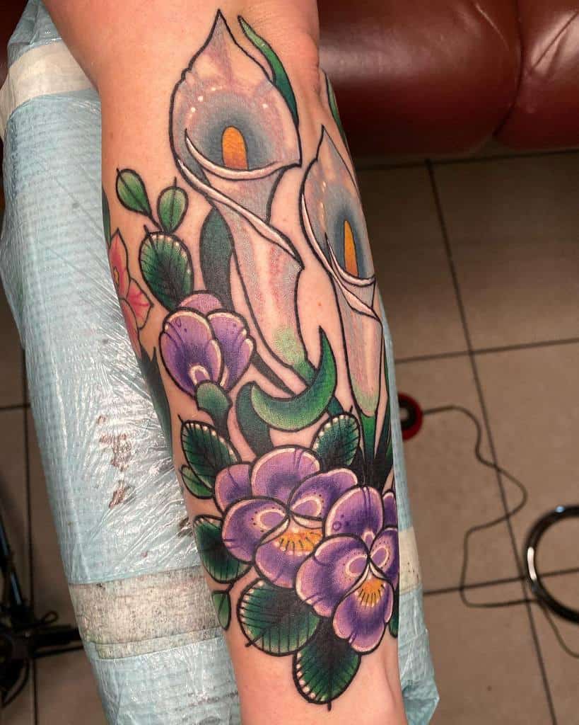 Vibrant tattoo of calla lilies and purple flowers elegantly adorns the outer forearm