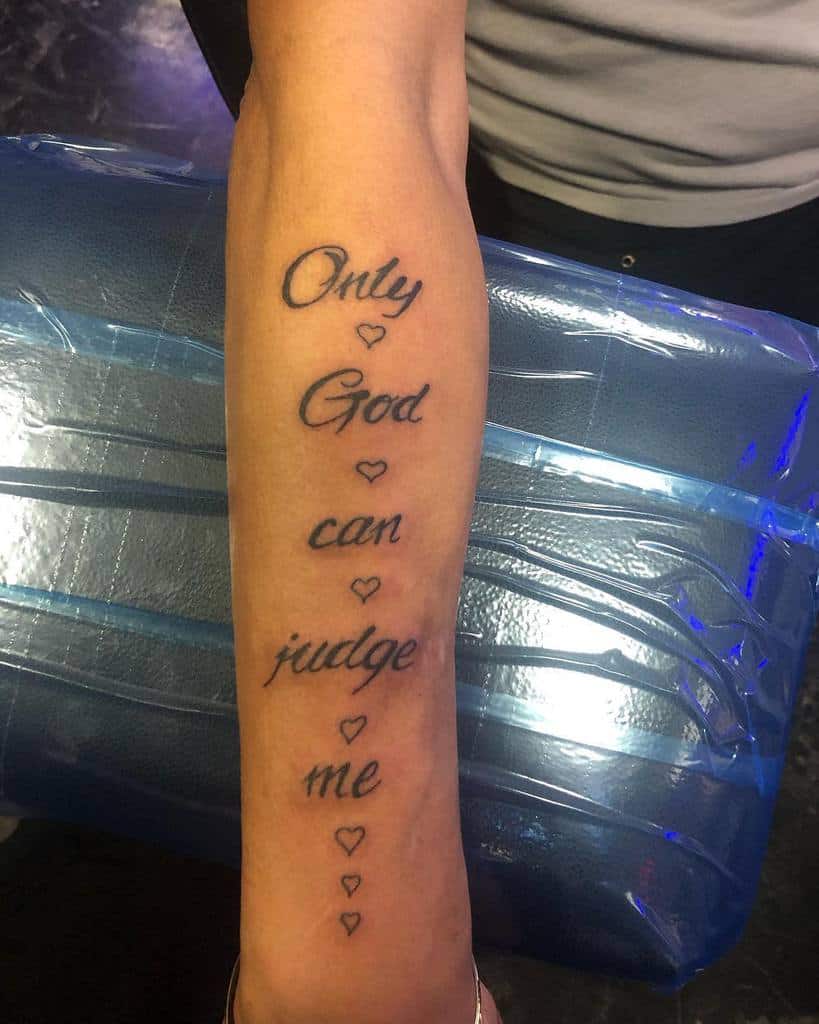 Outer forearm tattoo with the phrase 'Only God can judge me' written in script, accompanied by small hearts, symbolizing faith and personal conviction