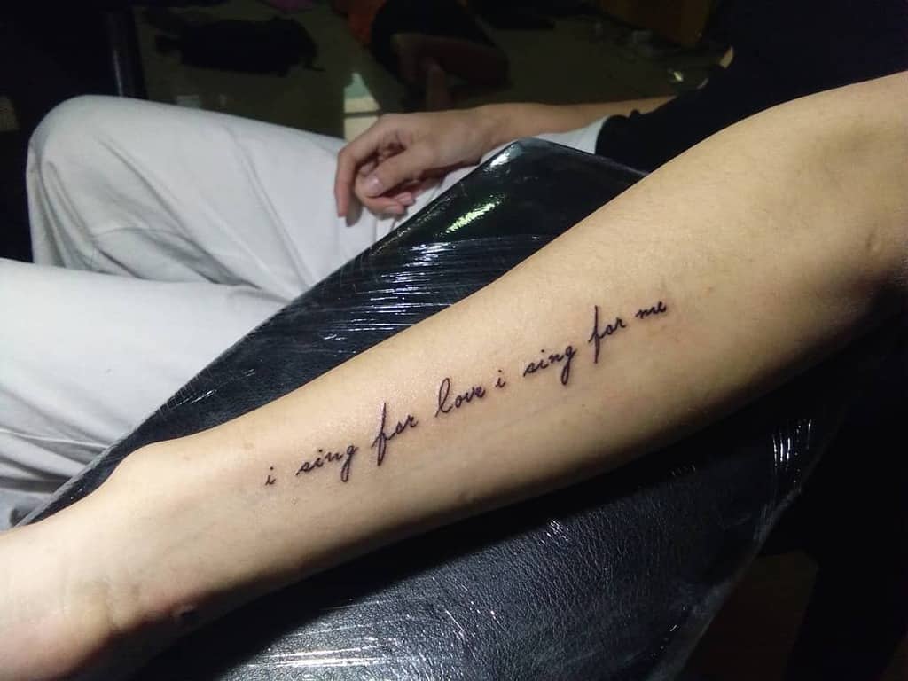 Tattoo on outer forearm beautifully reads "i sing for love i sing for me" in elegant cursive script