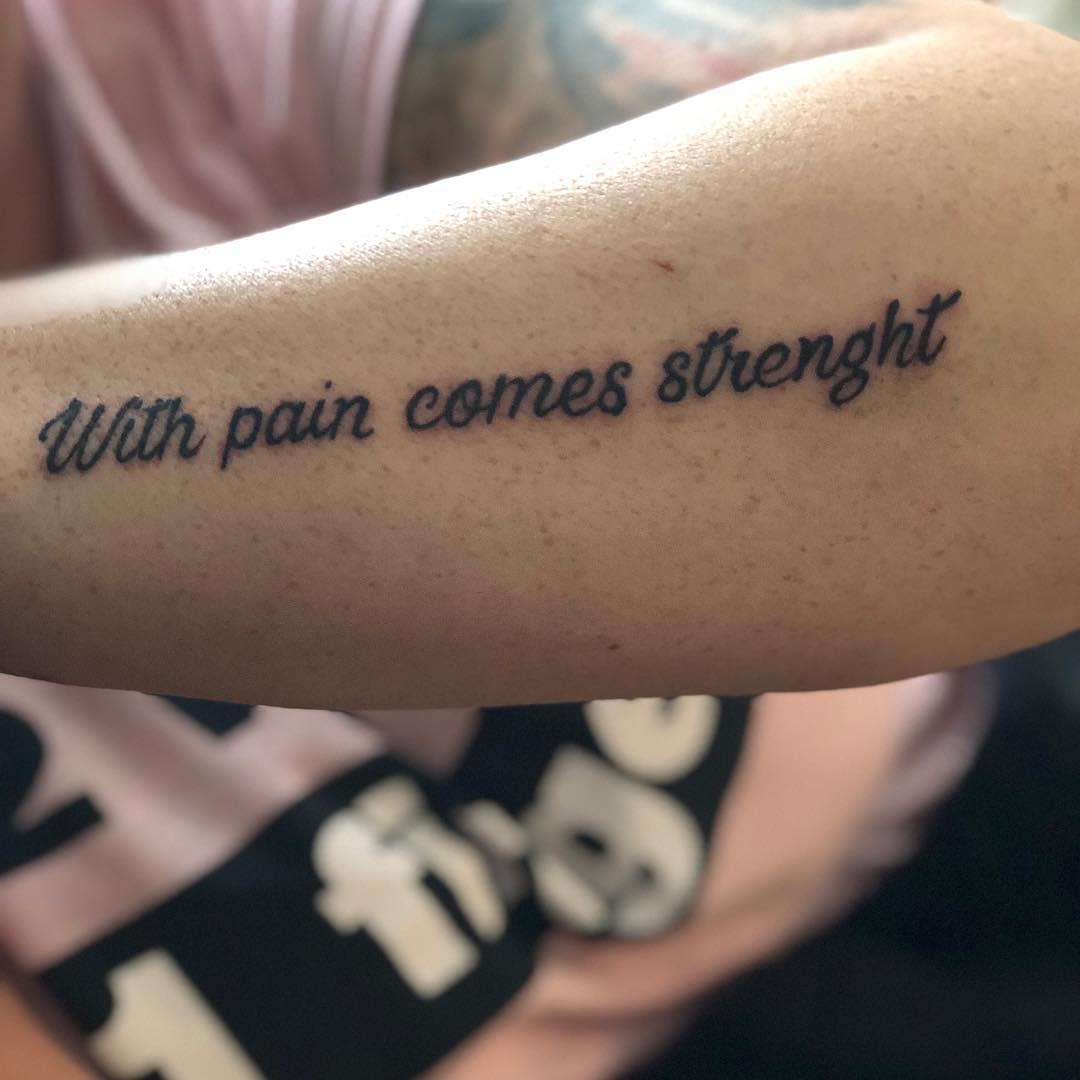 Outer forearm tattoo with the quote 'With pain comes strength' in cursive, symbolizing resilience and growth through adversity