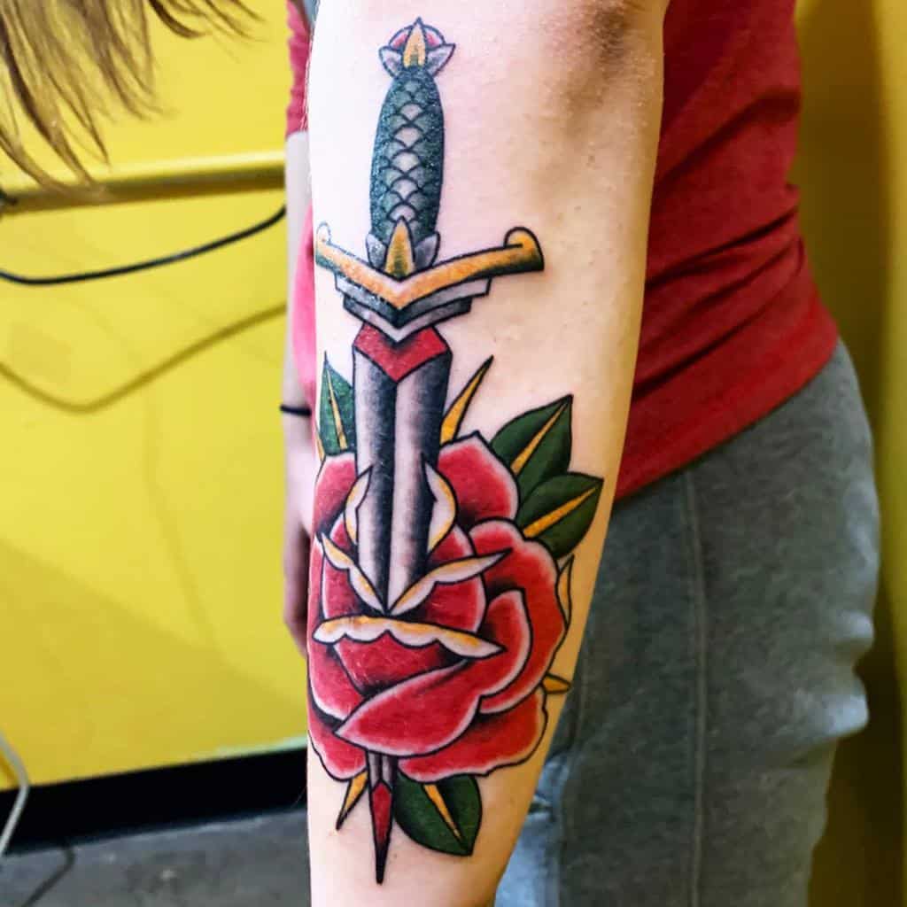 A tattoo of a sword piercing a rose on the outer forearm