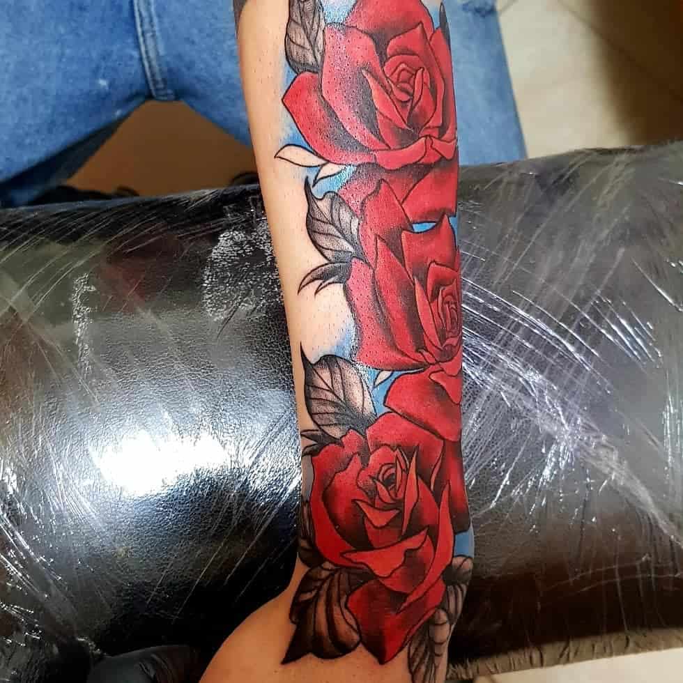 Tattoo of vibrant red roses with green leaves gracefully wrapping around the outer forearm