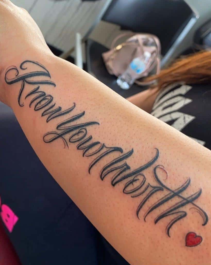 Tattoo on an outer forearm reading "Know Your Worth" with a small red heart