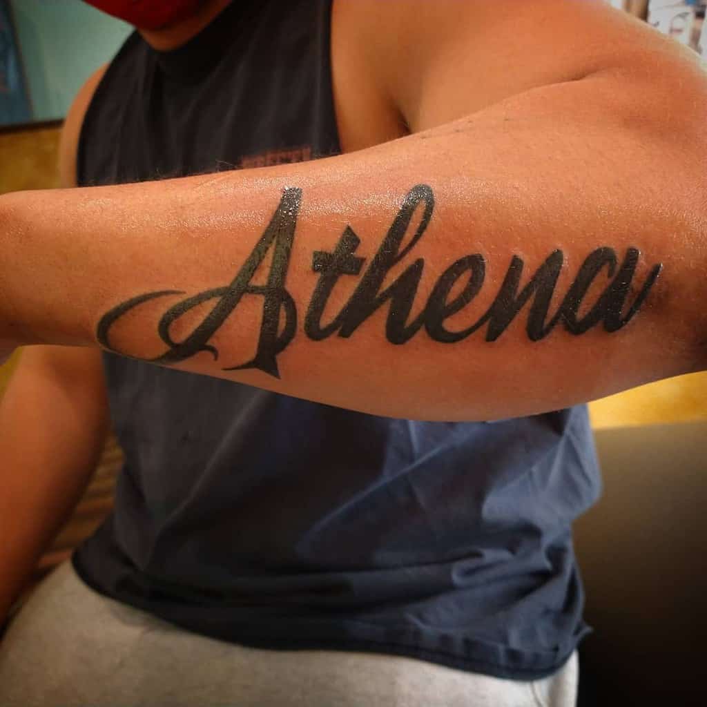 Outer forearm tattoo with the word "Athena" in bold, cursive script
