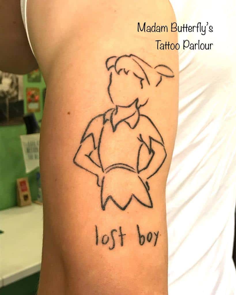 Minimalist line-art tattoo of Peter Pan with no facial features, hands on hips, and the phrase "lost boy" written underneath