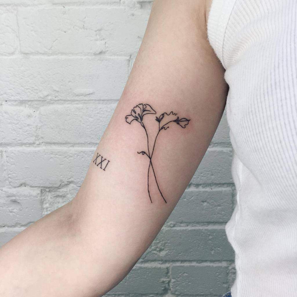A minimalist sweet pea tattoo with fine line detailing, paired with a simple Roman numeral XXI