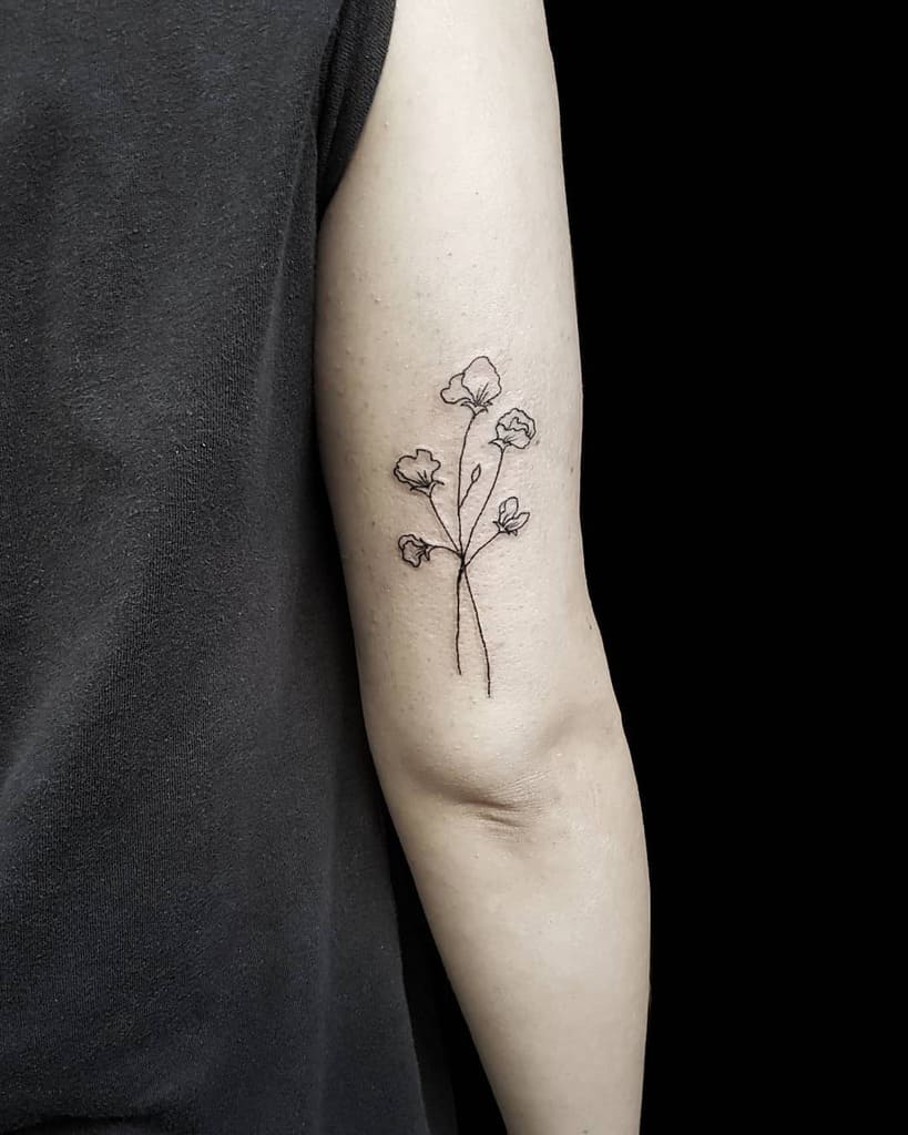A simple, fine-line sweet pea flower tattoo on the upper arm, showcasing natural elegance