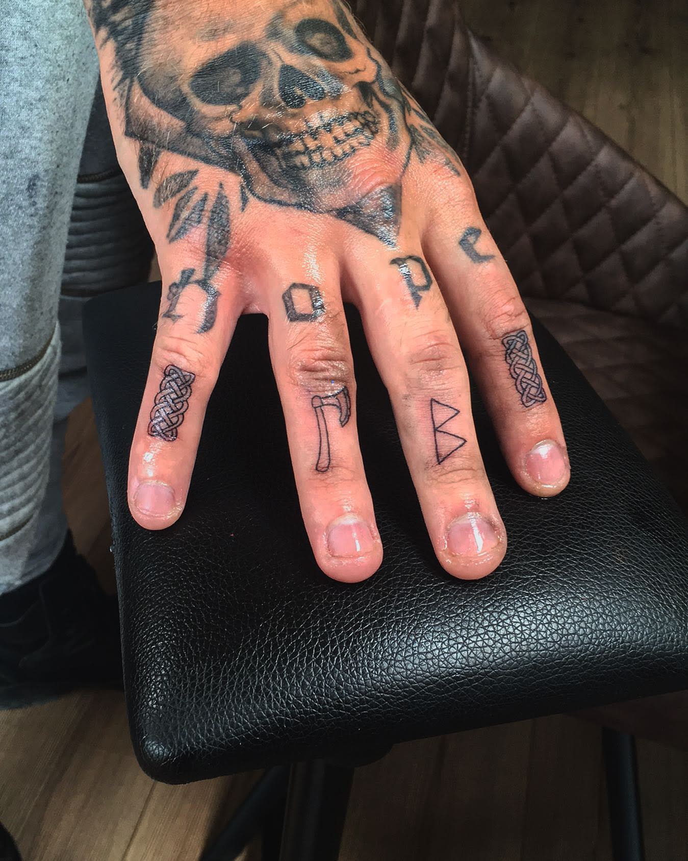 Close-up of a hand with "hope" and symbols tattooed on the fingers, a skull on the hand