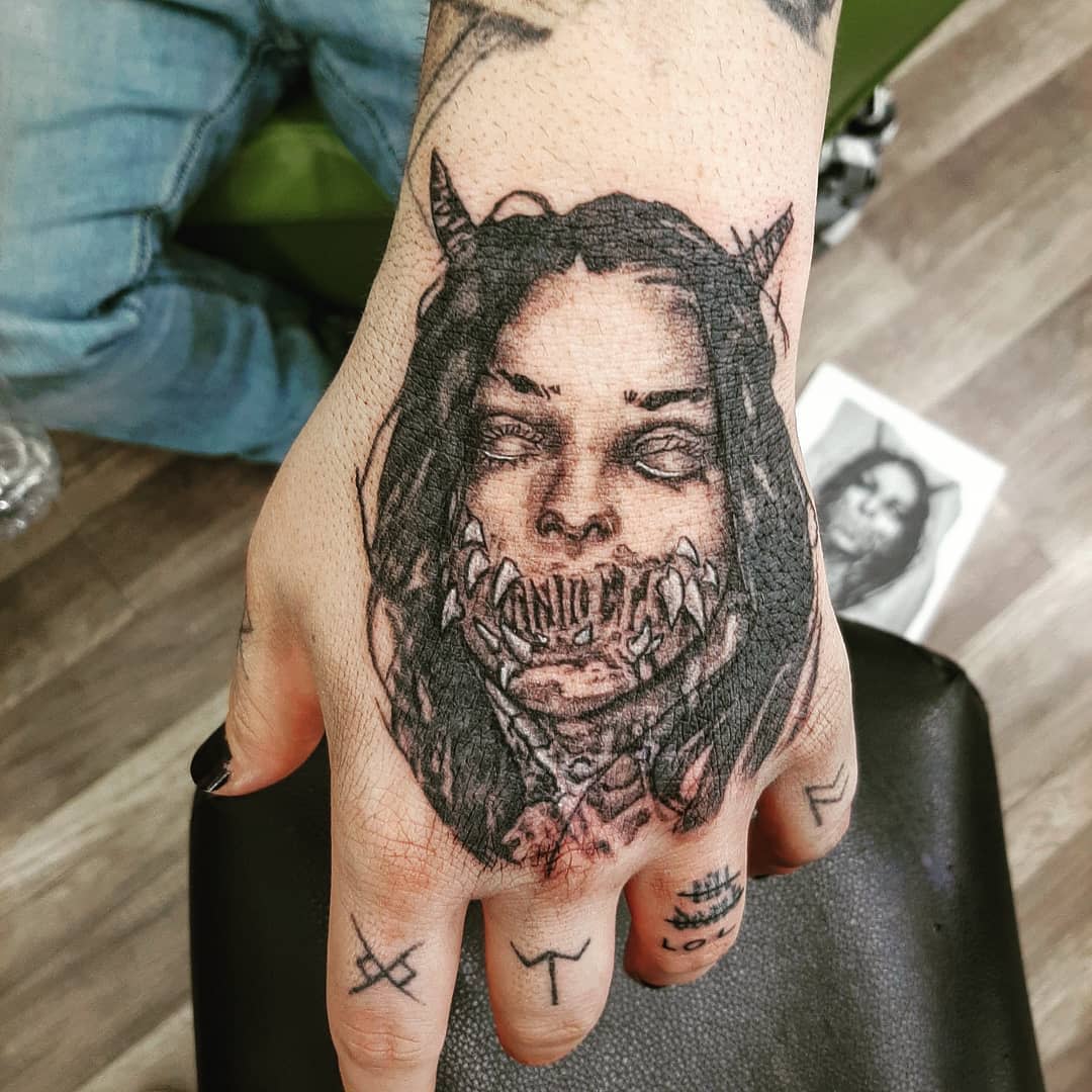 Tattooed hand featuring a demonic woman's face with horns and sharp teeth