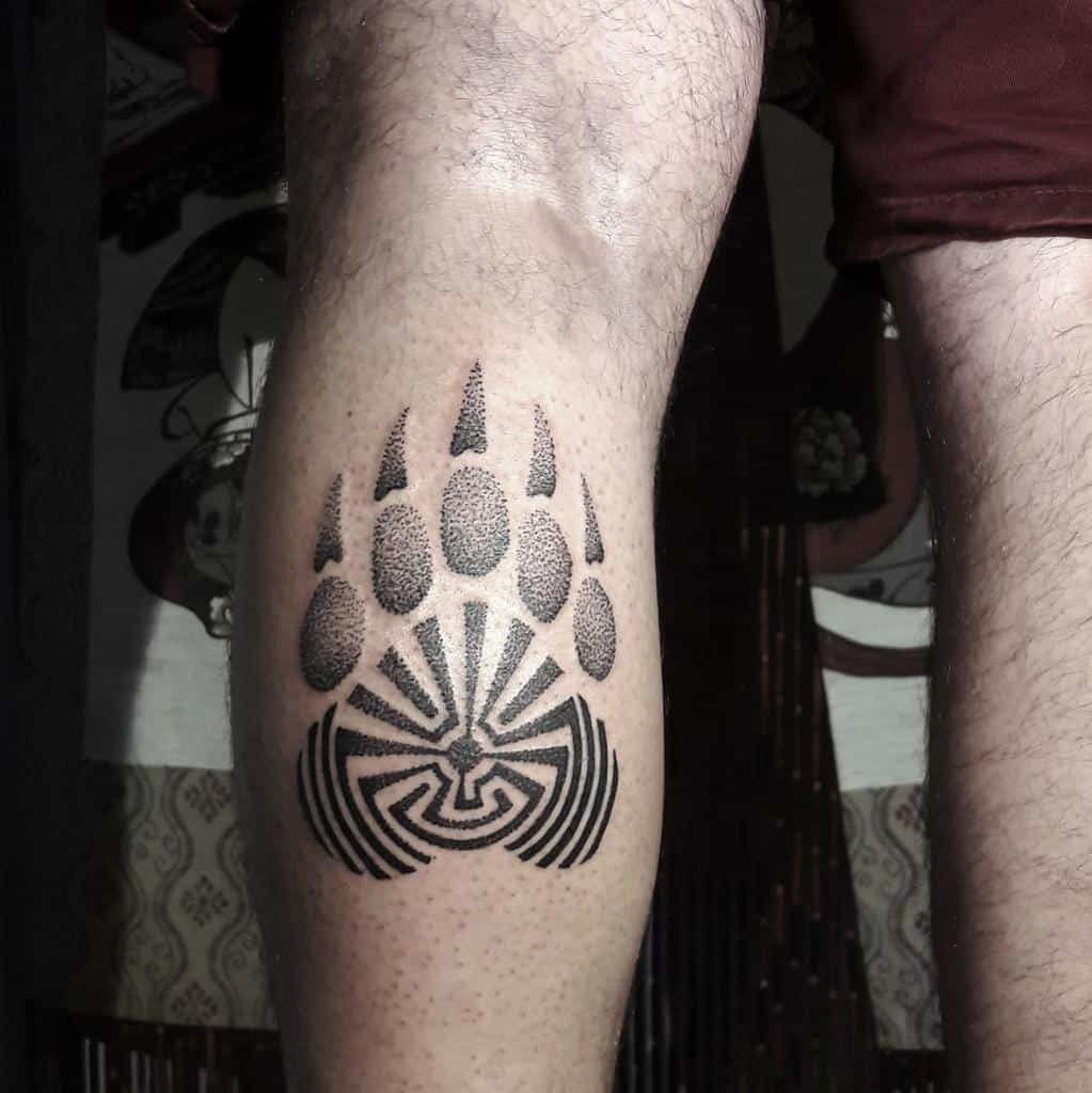 A geometric bear paw tattoo adorns a person's calf, featuring intricate, maze-like patterns that echo the strength and spirit of the bear itself