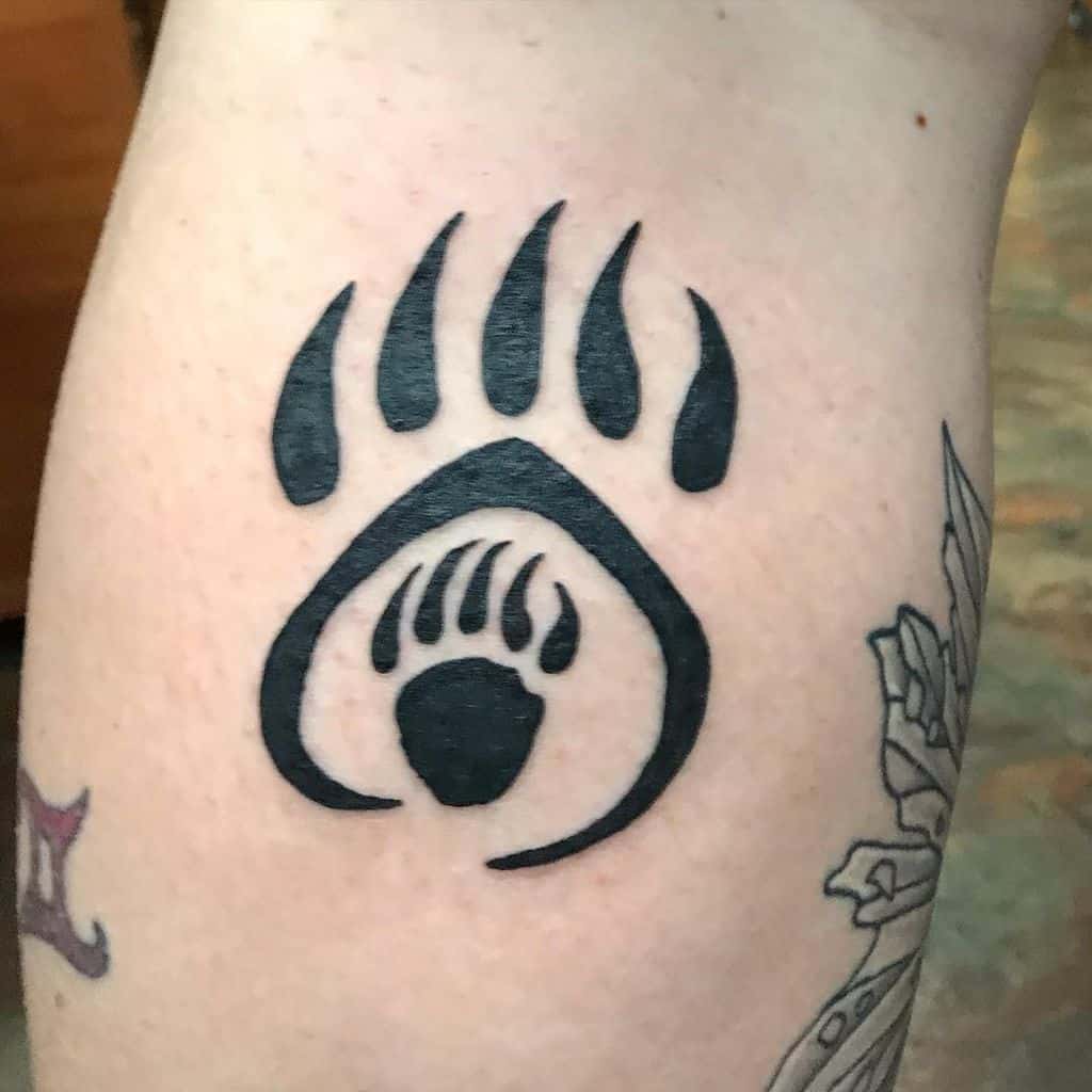 Bear-themed tattoo on upper arm, showcasing a large black bear paw with a smaller paw nestled inside it