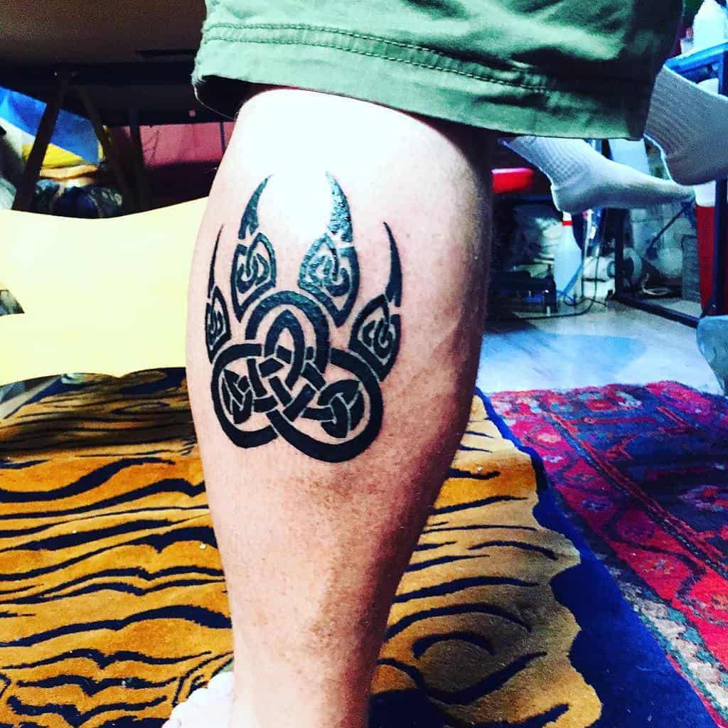 A striking tattoo of a Celtic knot bear paw adorns a leg