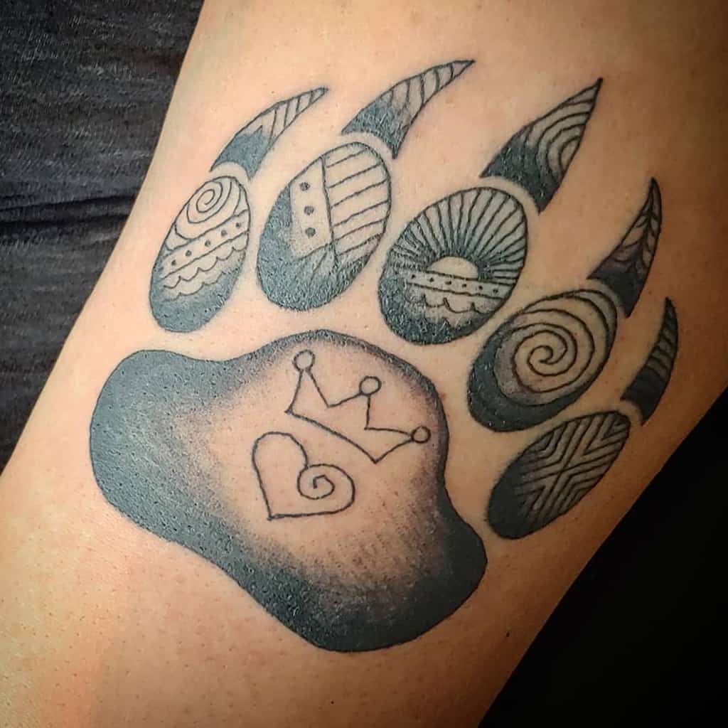 Tattoo of a bear paw print with intricate patterns, featuring a majestic crown and heart symbol in the center pad, embodying the spirit of the bear