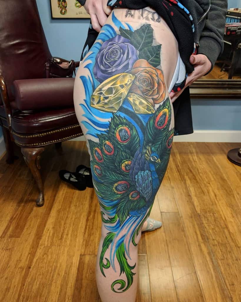 Colorful peacock and rose tattoo covering a woman's side and thigh