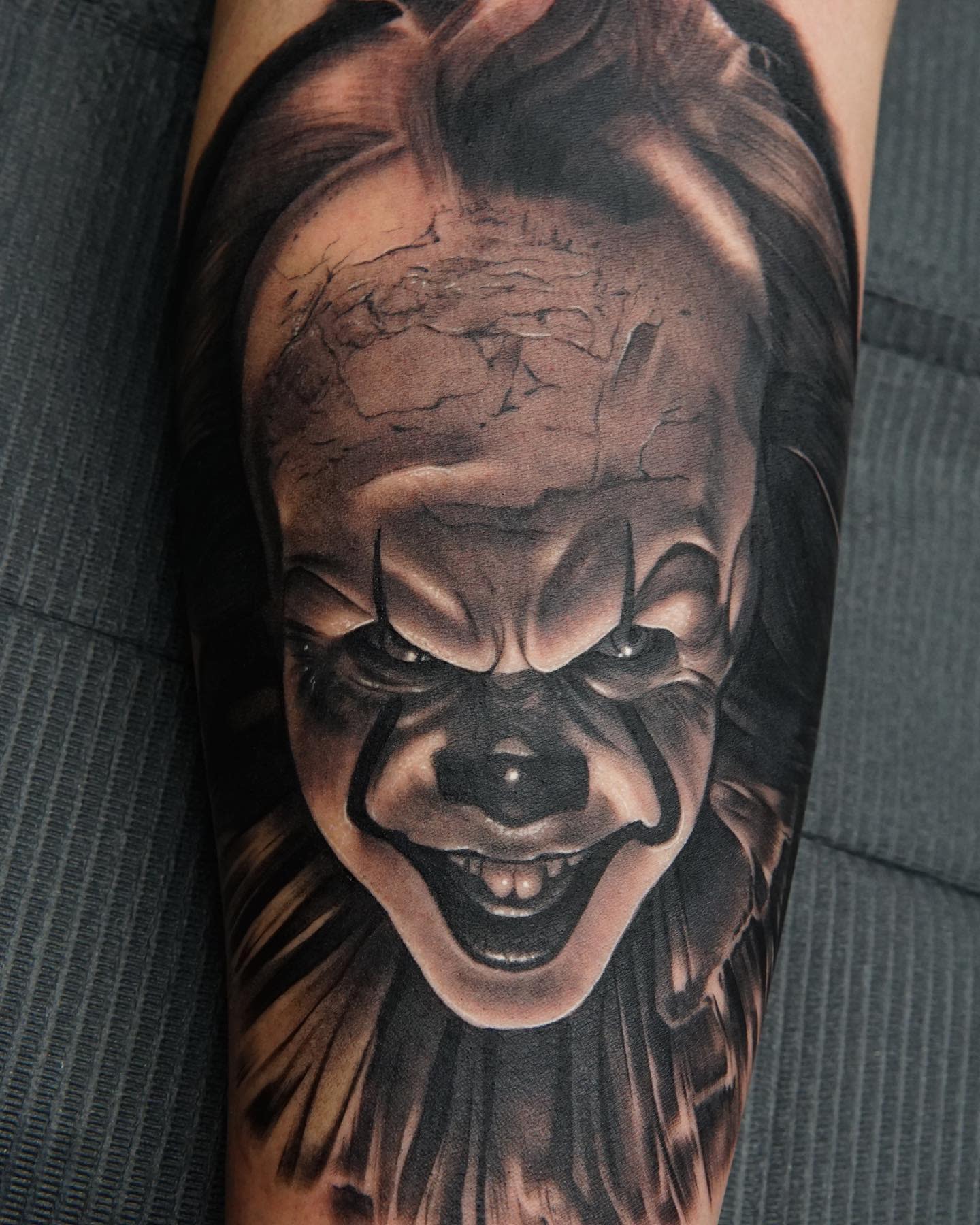Pennywise tattoo with detailed shading on upper arm, showing his sinister expression