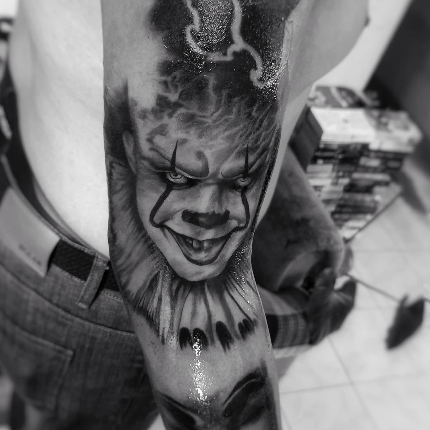 Pennywise tattoo with detailed shading on upper arm, showing his sinister expression