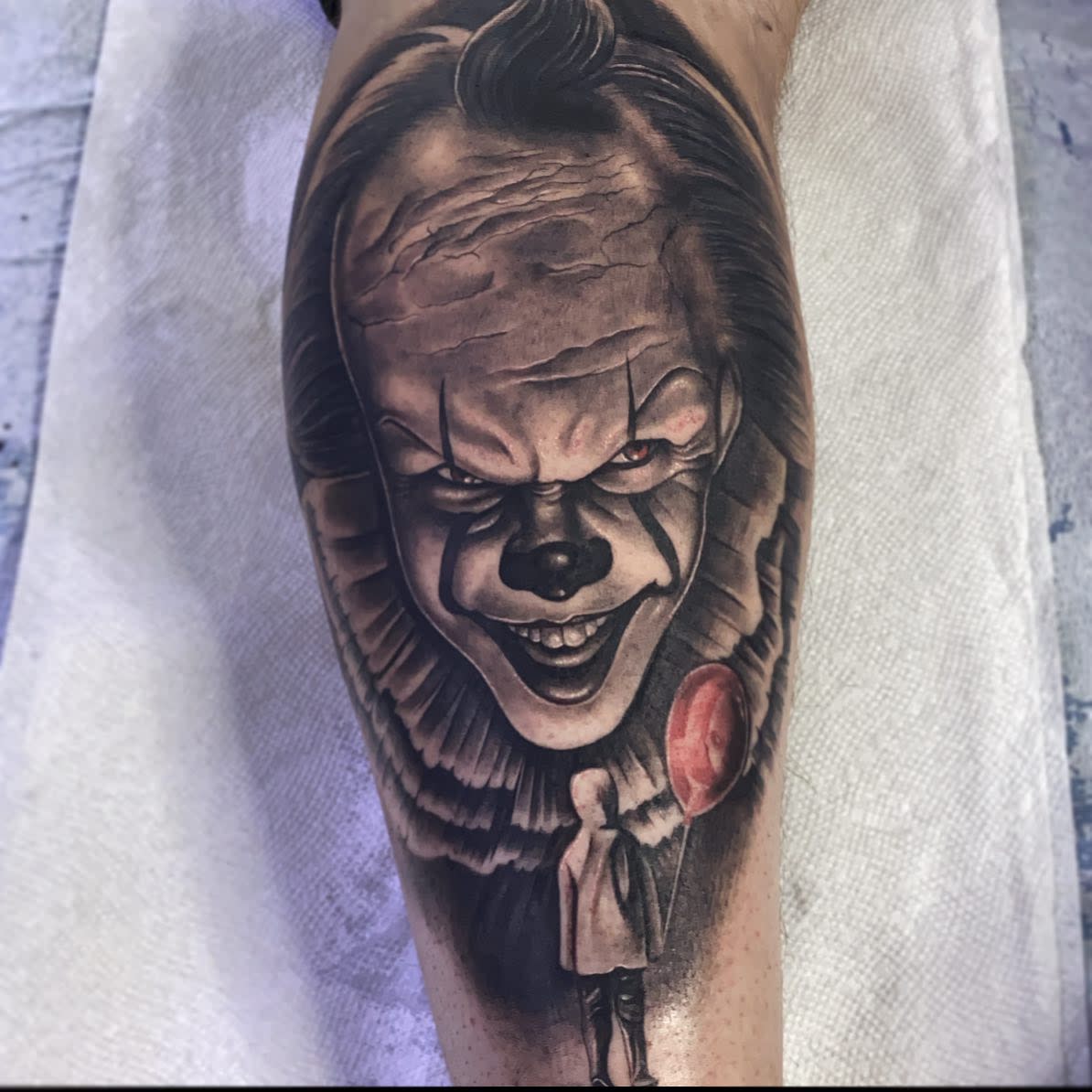 Pennywise tattoo featuring his iconic grin and a red balloon, symbolizing fear