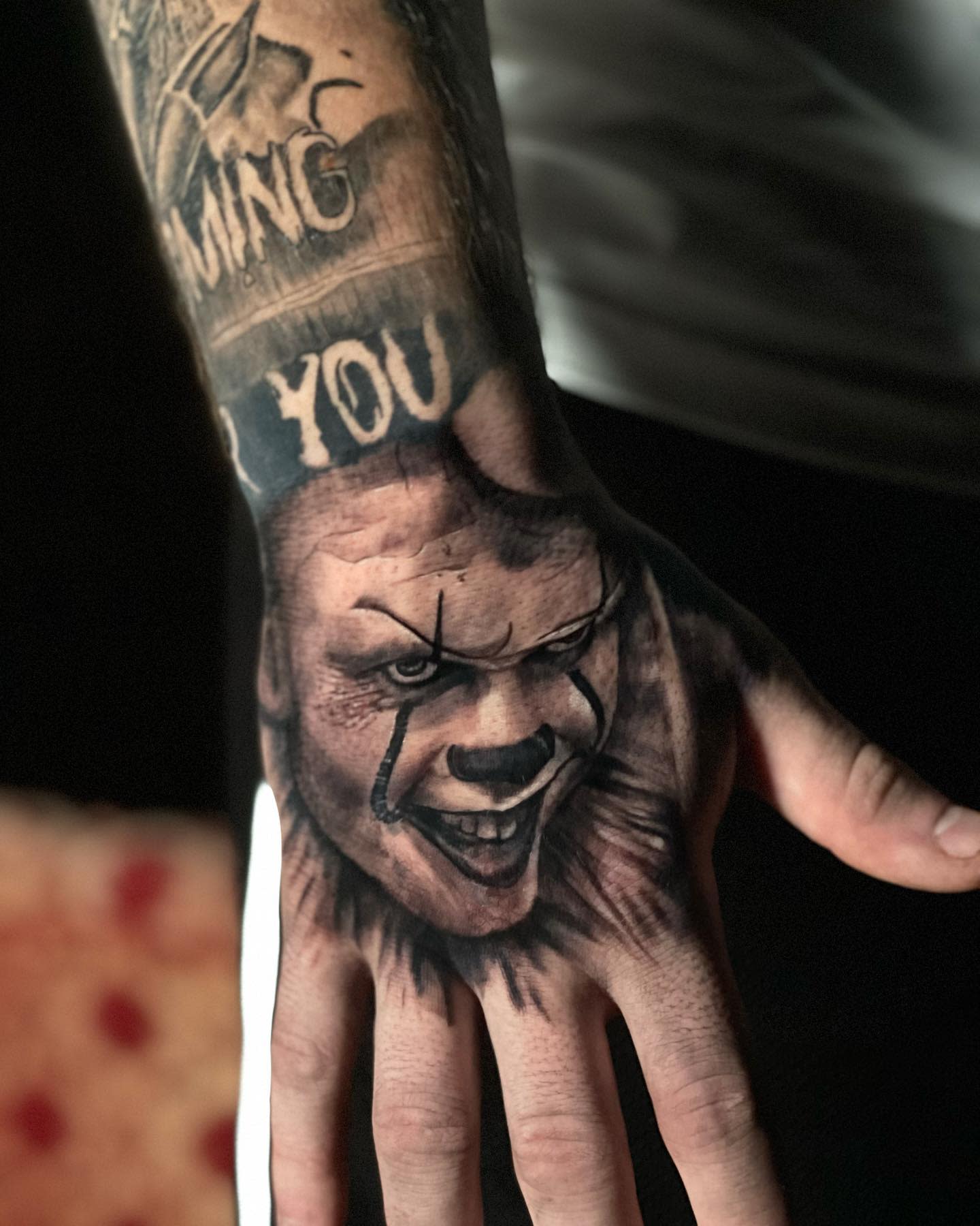 Detailed Pennywise tattoo on hand, with a haunting smile and dark shadows