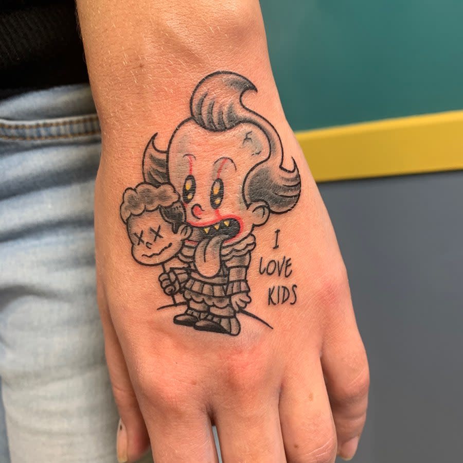 Cartoon-style Pennywise tattoo on hand, with exaggerated features and bright colors