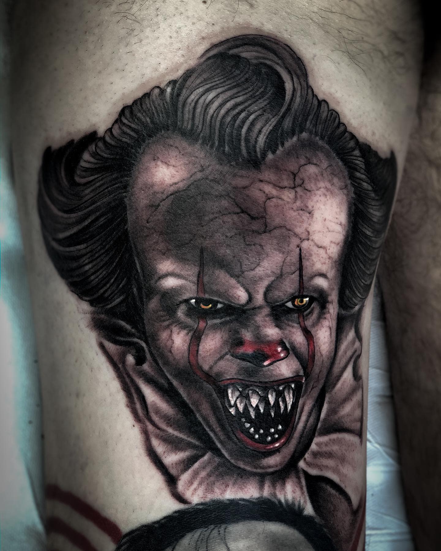 Hyper-realistic Pennywise tattoo on thigh, showcasing his terrifying grin and sharp teeth
