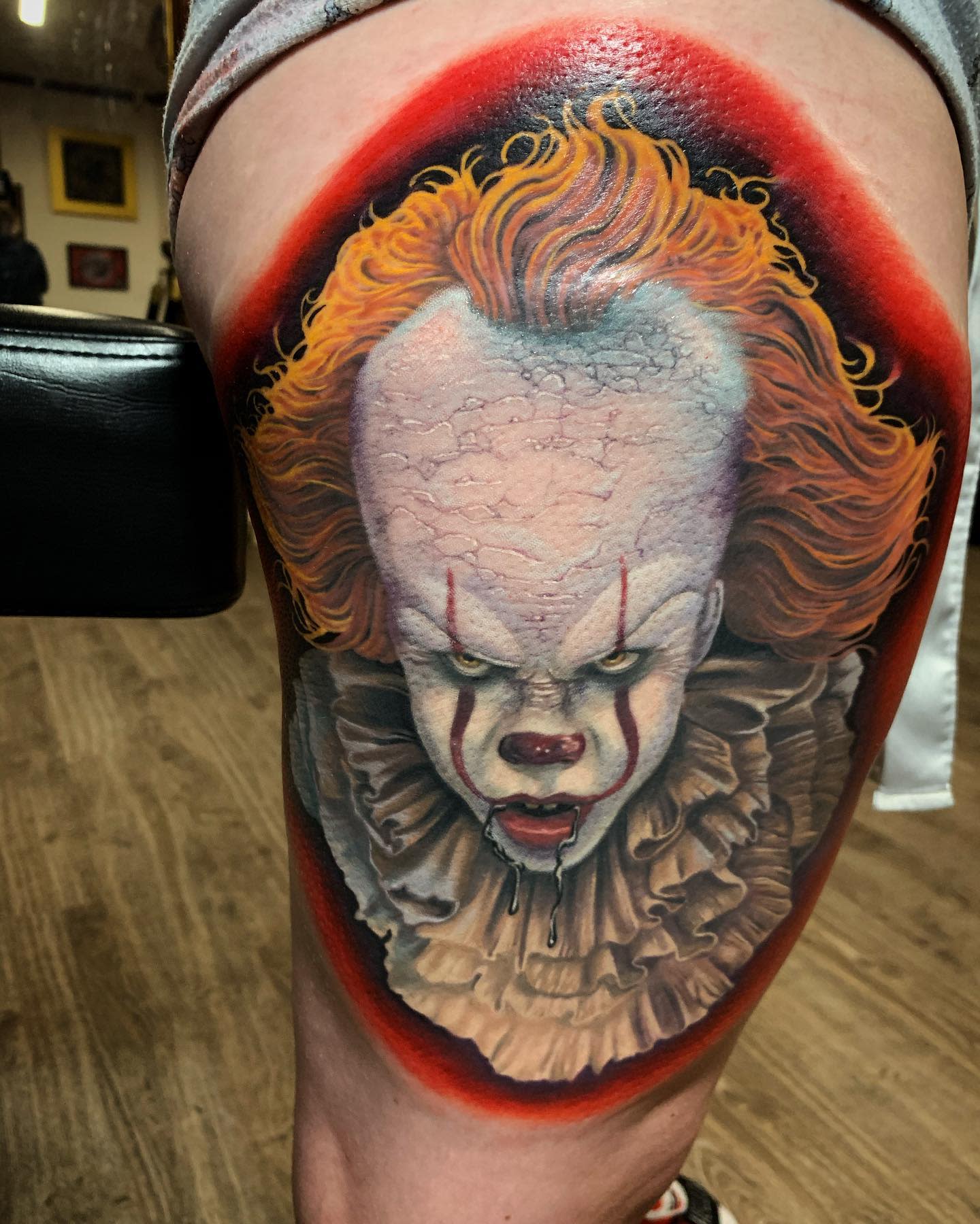 Vibrant Pennywise tattoo on thigh, highlighting his fierce expression and fiery orange hair