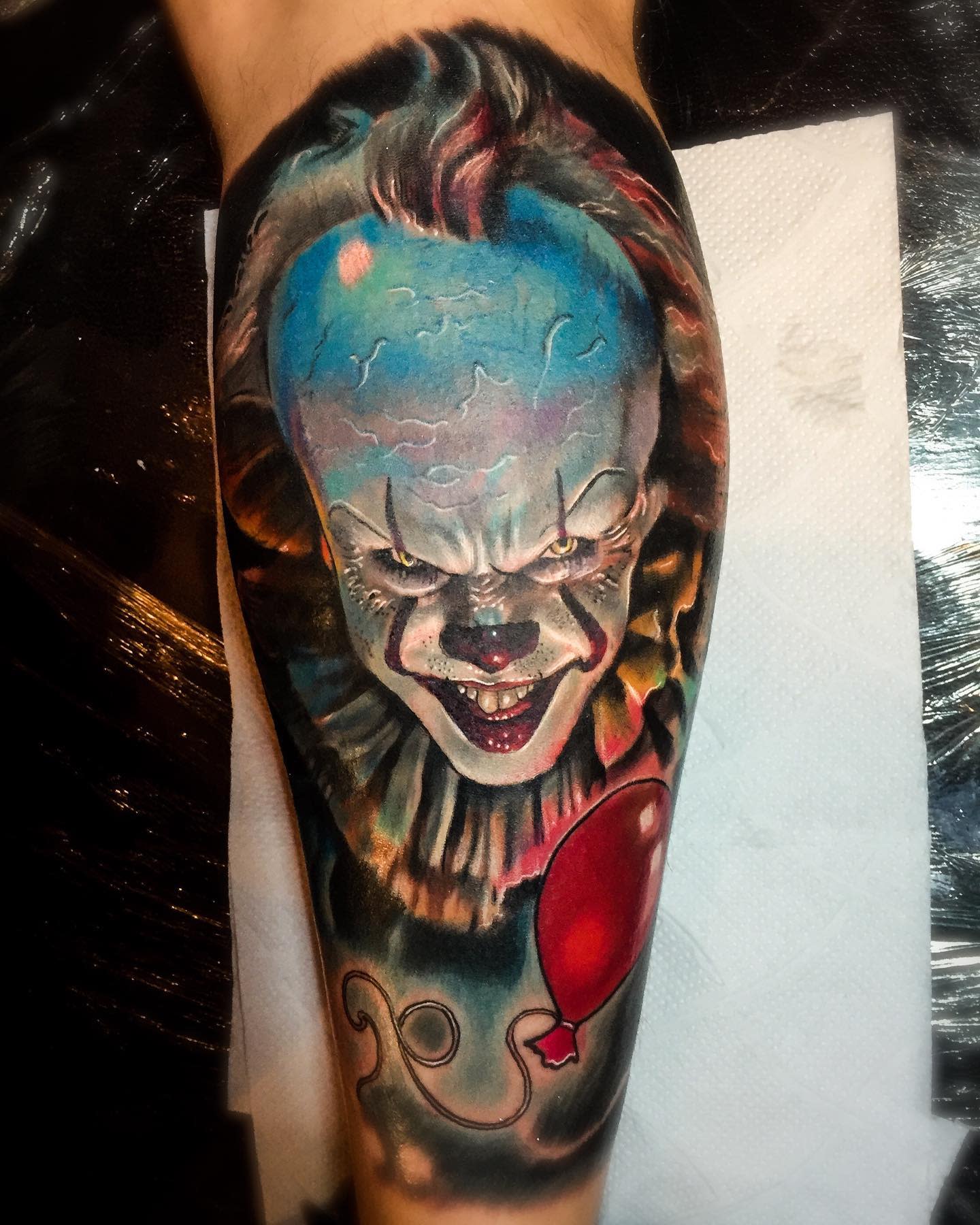 Realistic Pennywise tattoo on leg, featuring his eerie grin and iconic red balloon