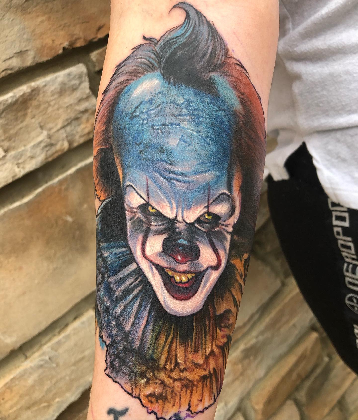 Colorful Pennywise tattoo on forearm, capturing his menacing smile and detailed facial features