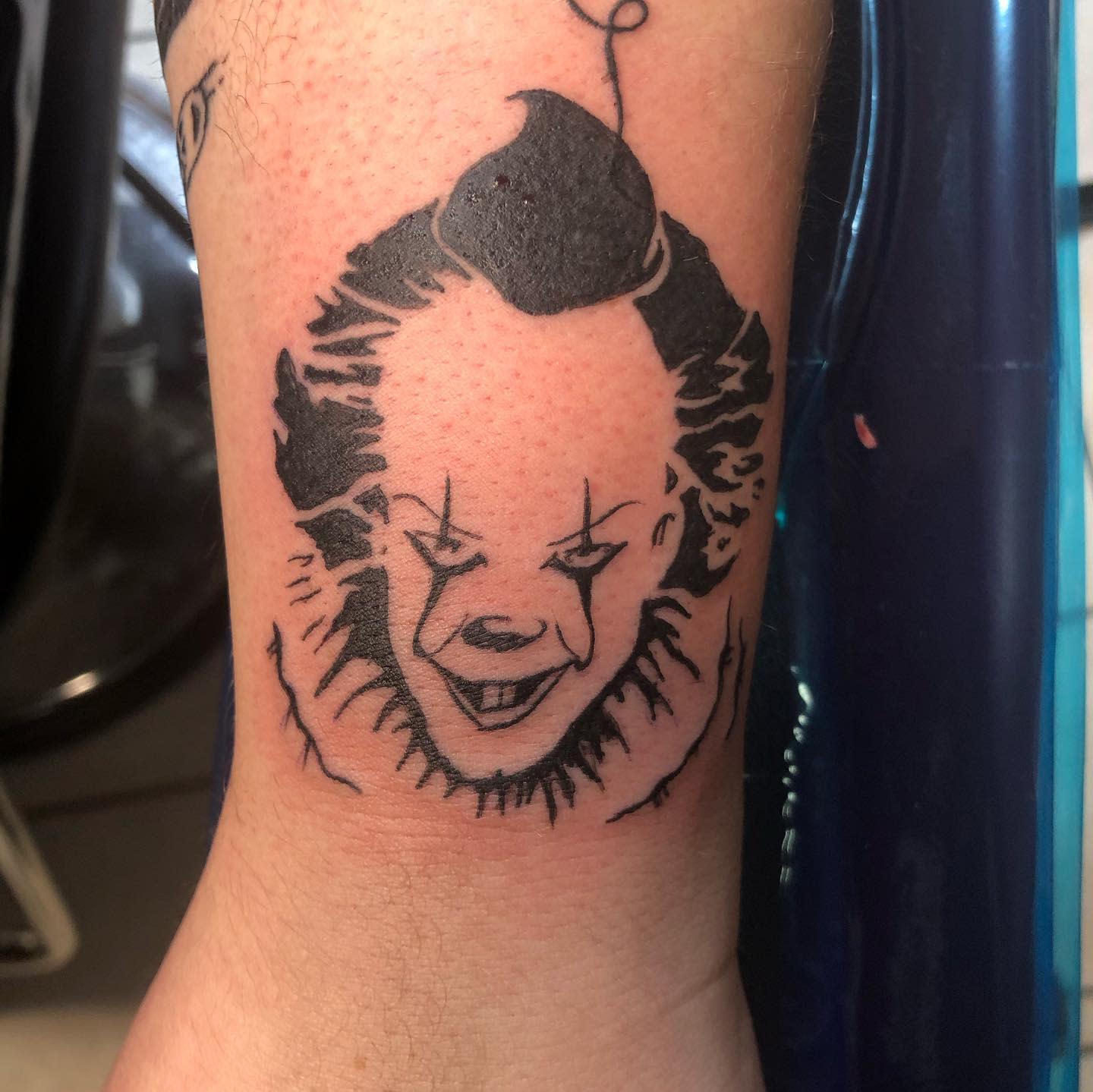 Minimalist Pennywise tattoo on wrist, featuring a simple black outline and a small balloon