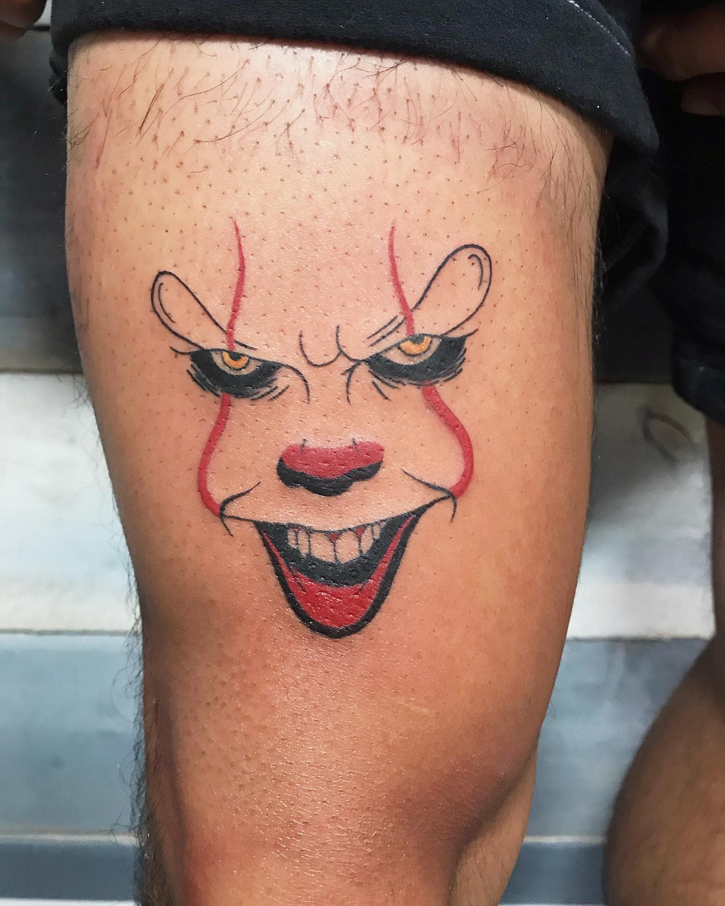 Small Pennywise face tattoo on leg, using minimal lines and color for a striking effect.