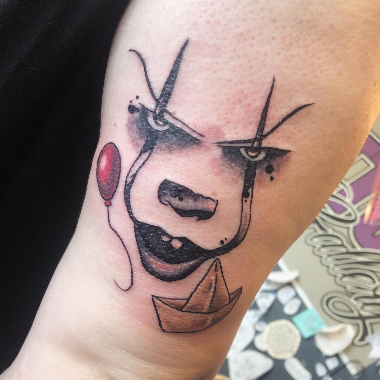 Minimalist Pennywise tattoo with red balloon and paper boat, combining simplicity with eerie details