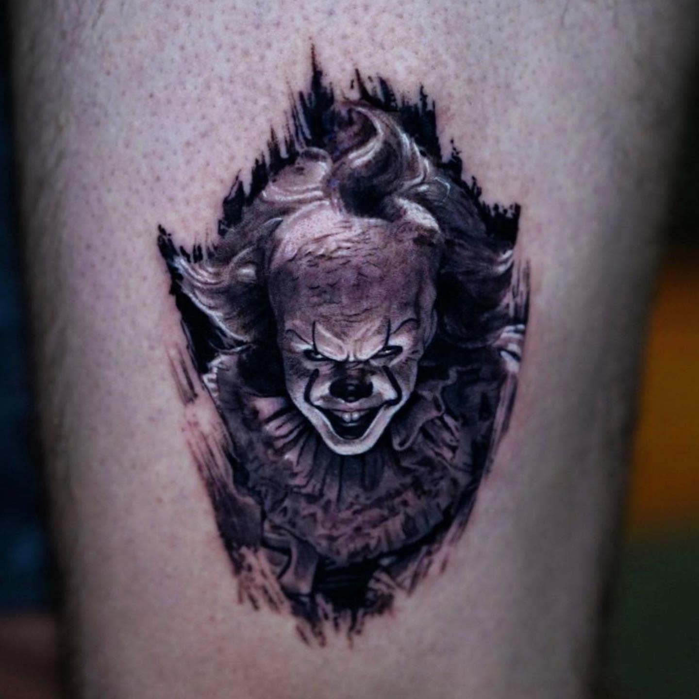 Small black and grey Pennywise tattoo with a dramatic, shadowy background, highlighting his eerie grin