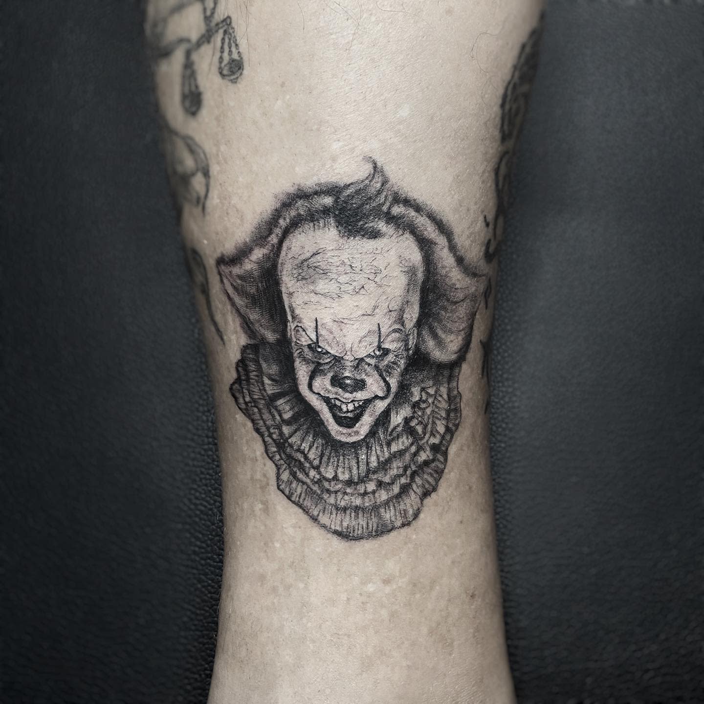 Small, detailed Pennywise tattoo on leg, featuring his menacing grin and intricate shading