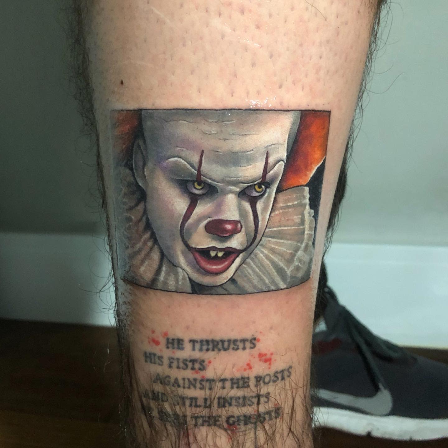 Small, vibrant Pennywise tattoo on leg, with intense expression and accompanying text below