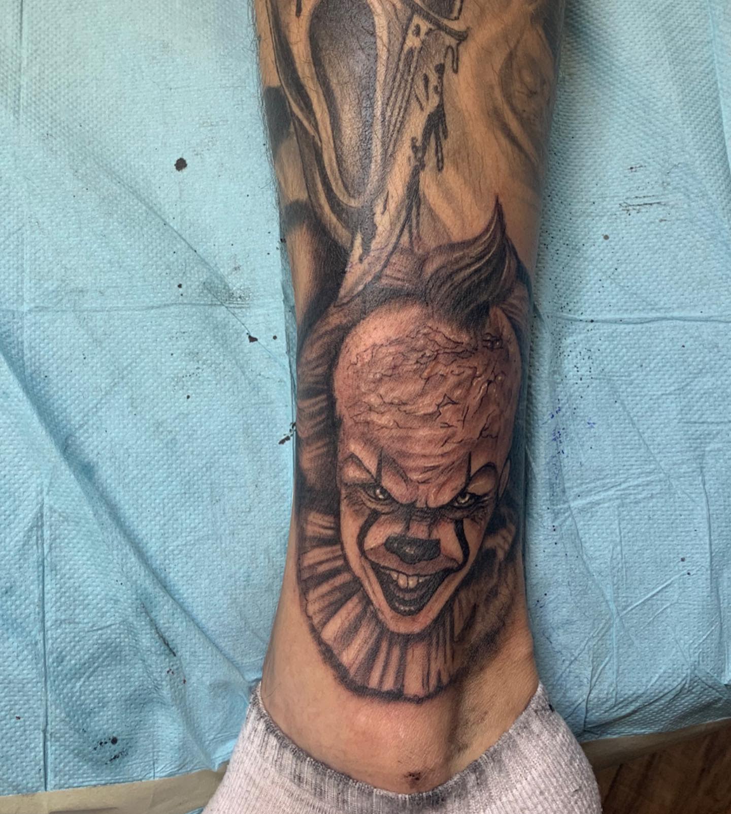 Small Pennywise tattoo on leg with detailed shading, capturing his sinister grin and intense eyes