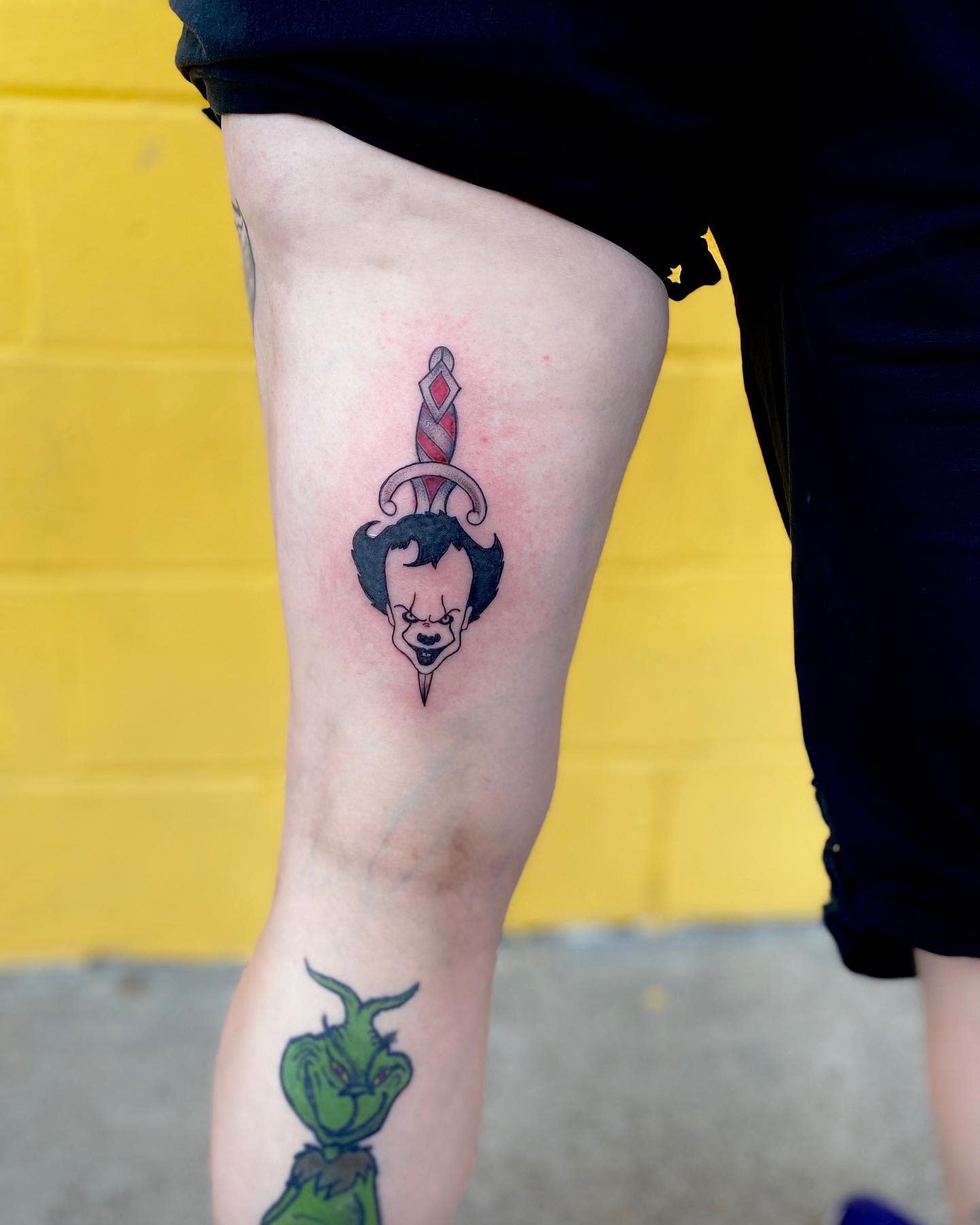 Small Pennywise tattoo with a dagger design, featuring a simplified version of Pennywise's face integrated into the dagger, located on the upper thig