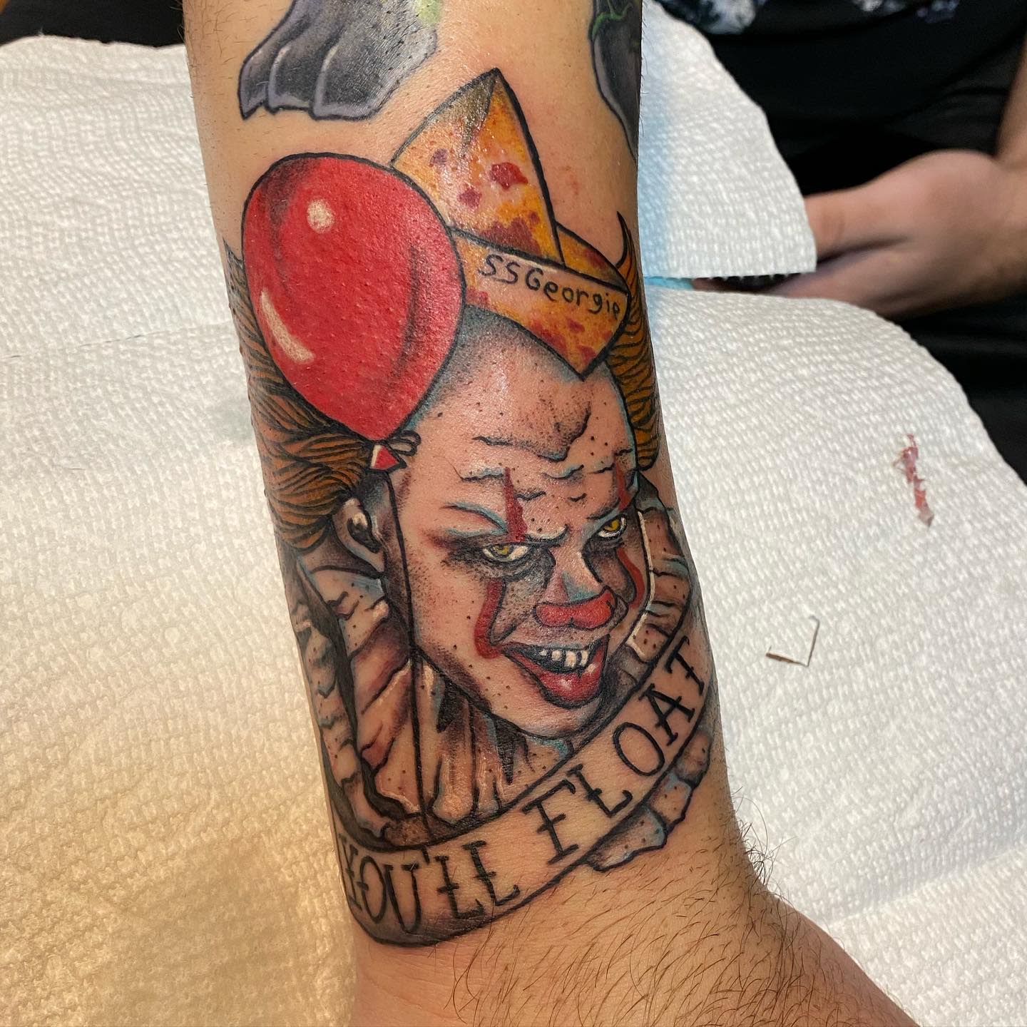 A traditional-style Pennywise tattoo with a red balloon, "SS Georgie" paper boat, and "You'll Float" text