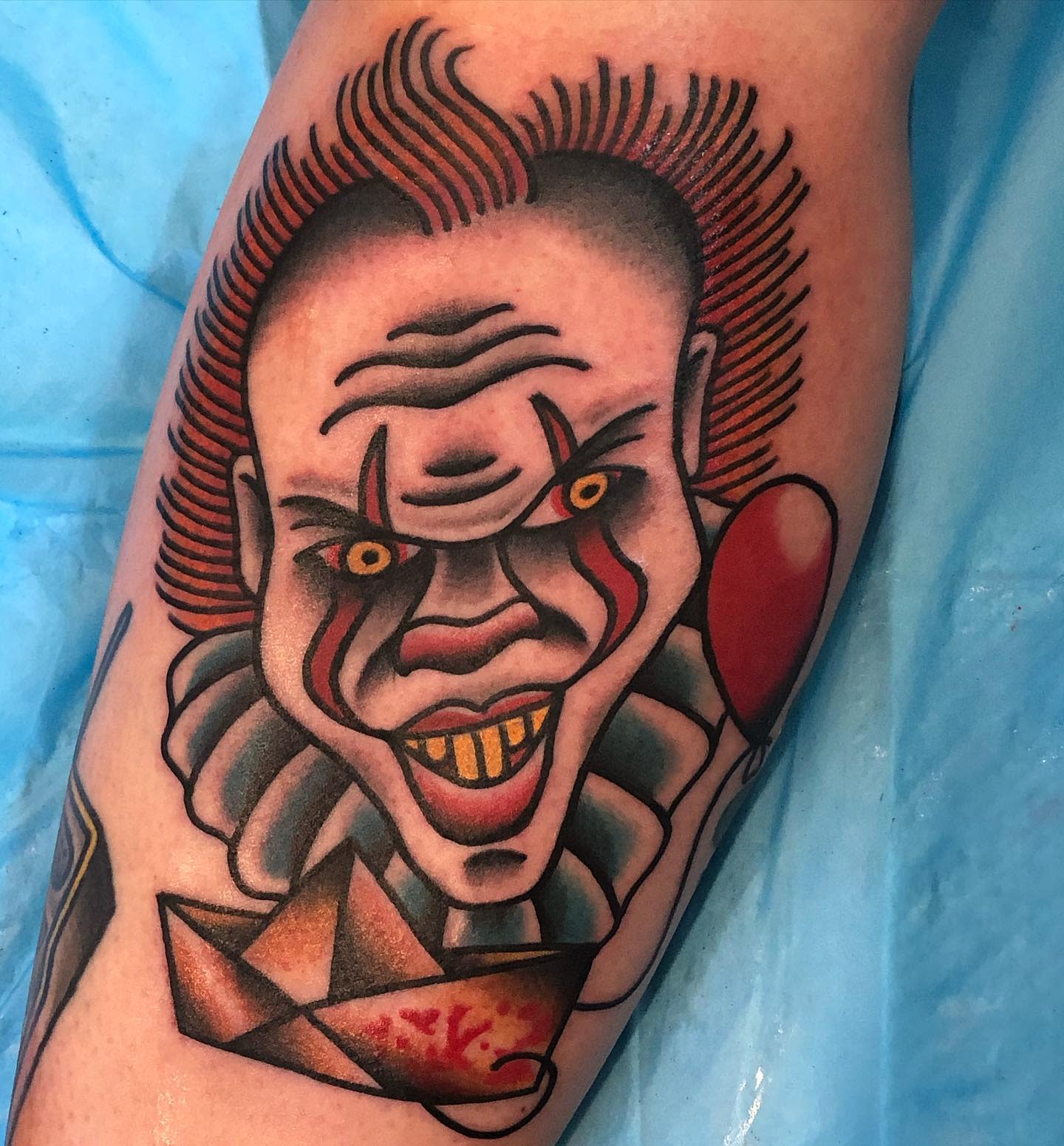 A traditional-style Pennywise tattoo with a menacing expression, red balloon, and "SS Georgie" paper boat