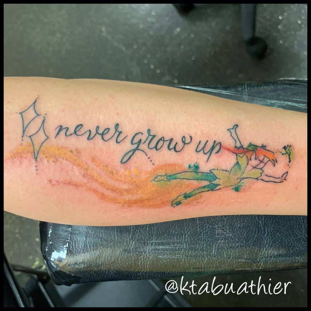 Tattoo of Peter Pan flying with the text "never grow up" and two small stars