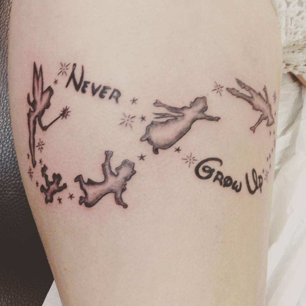 Whimsical 'Never Grow Up' tattoo with Tinker Bell, Peter Pan, Wendy, and the Darling children flying in a magical starry design