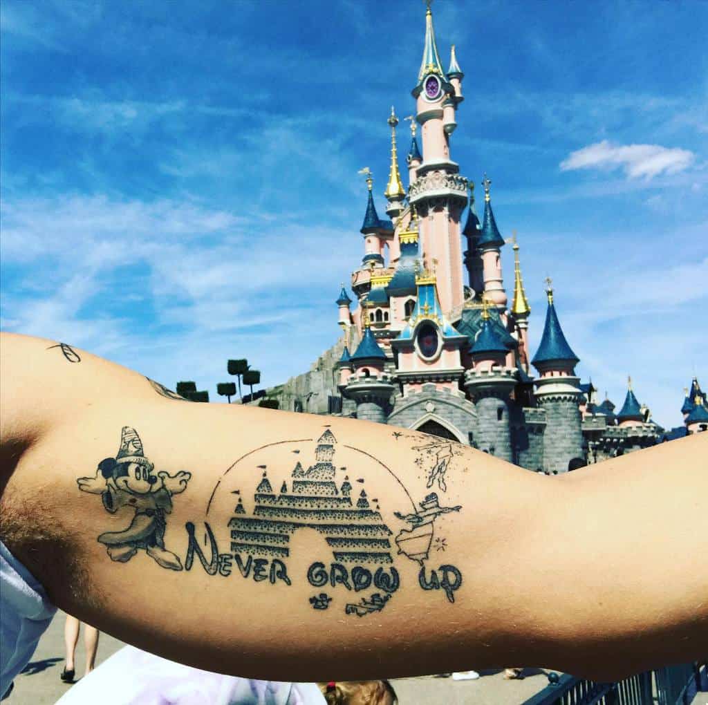 Disney-inspired 'Never Grow Up' tattoo featuring Mickey, Tinker Bell, a castle, and Peter Pan magic