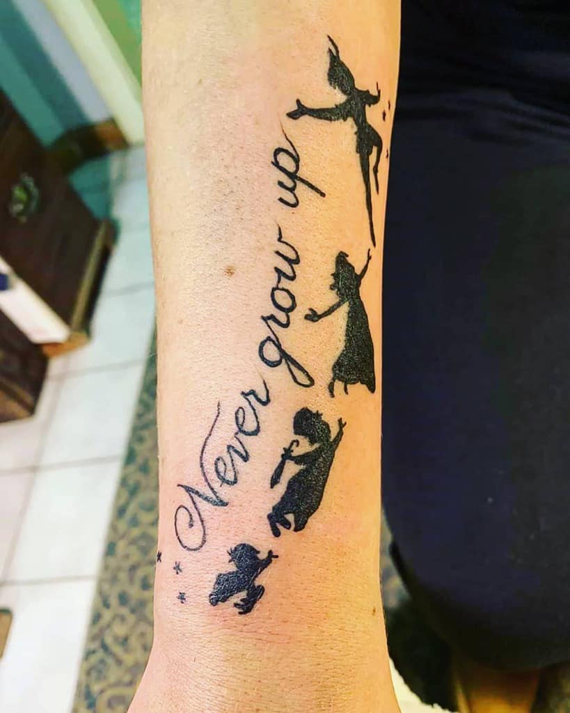 A tattoo with Tinker Bell, Peter Pan, Wendy, and the Darling children flying with the phrase "Never grow up" in cursive