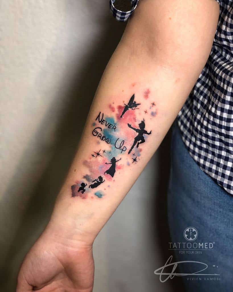Watercolor-style tattoo of Peter Pan, Tinker Bell, Wendy, John, and Michael flying among stars, with the phrase "Never Grow Up"