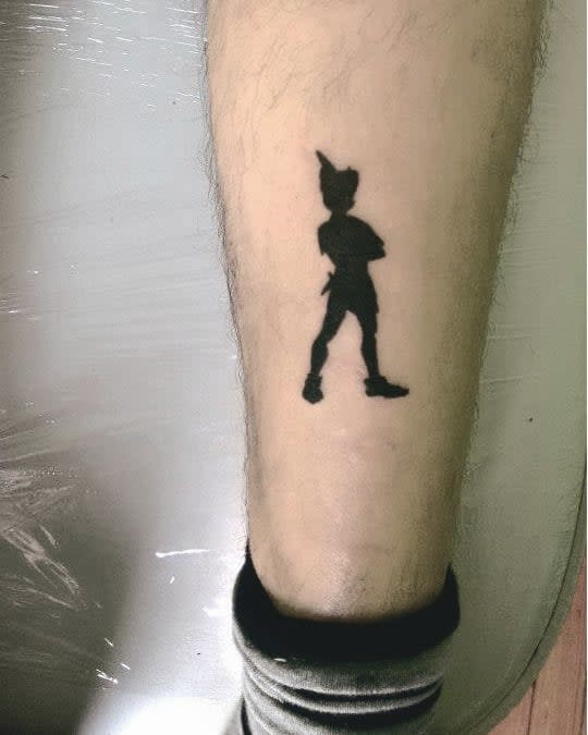 Black silhouette tattoo of Peter Pan standing confidently with arms crossed, symbolizing adventure and never growing up